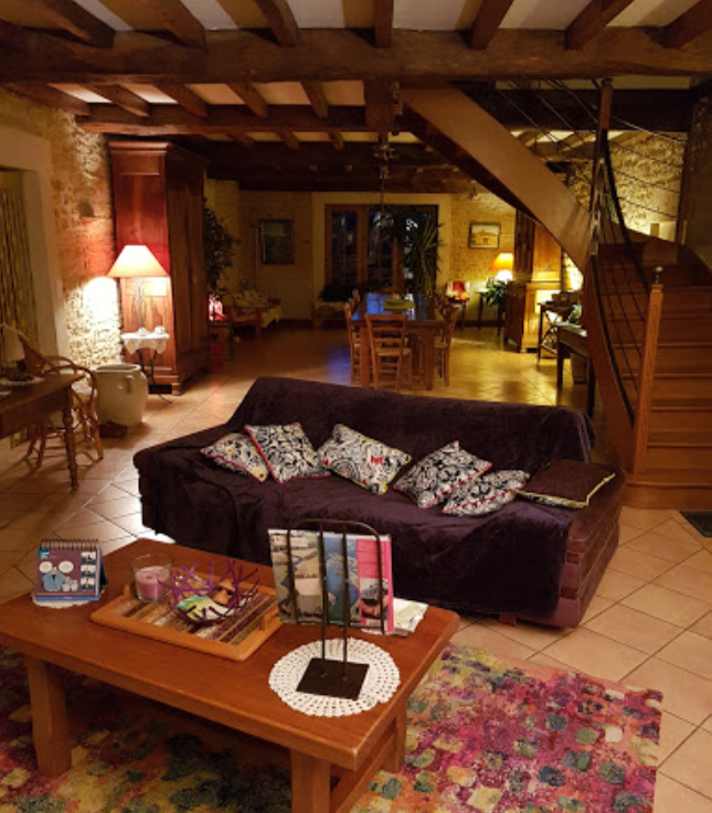 Salon intime avec canapé confortable, poutres en bois et éclairage doux dans une maison d'hôtes rustique.