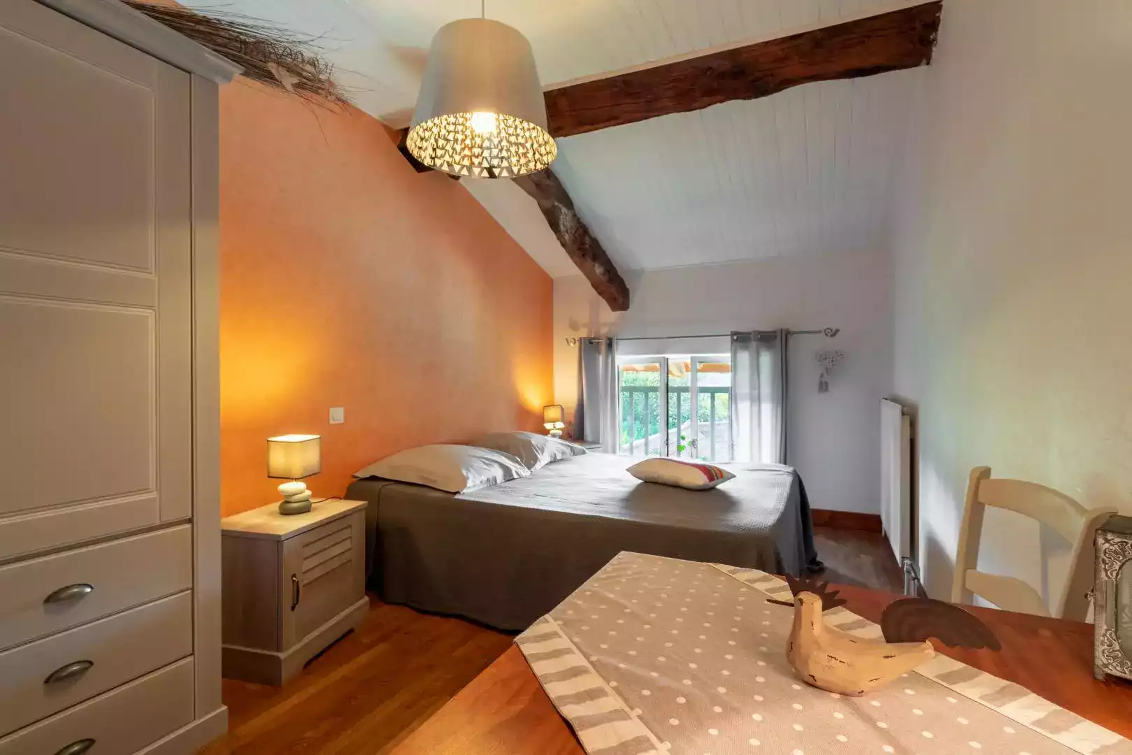 Chambre douillette avec linge de lit gris, poutres apparentes et lumière tamisée, offrant une atmosphère chaleureuse à L'agnoblens.